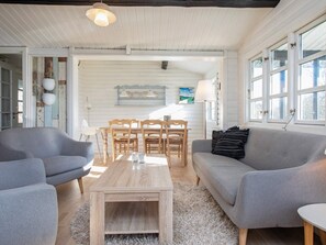 A living room with a wooden coffee table, grey sofas, a dining table with chairs, and a large window with multiple panes. - 7 Person Holiday Home in Vig (Vig)
