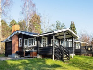 A log cabin with a chimney, a porch, and a staircase leading to a deck.