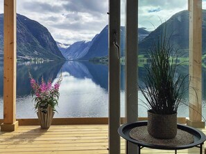 A room with a large window offering a view of a lake and mountains. There is a wooden floor and a potted plant on a small table. - 8 Person Holiday Home in Skei i Jolster (Sunnfjord)