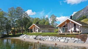 A lakeside cabin with a covered porch and a deck, surrounded by trees and a rocky shoreline. - 8 Person Holiday Home in Skei i Jolster (Sunnfjord)