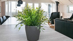 Ein modernes Interieur mit einem großen Tisch, einer Topfpflanze und Blick ins Freie durch große Fenster.