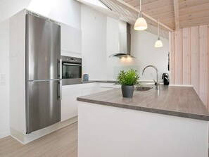 Cozinha moderna com eletrodomésticos de aço inoxidável, teto de madeira e iluminação pendente.