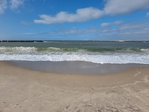 A beach with waves approaching the shore, a clear sky, and a distant landmass. - Holiday Home in HarboÃ¸re (Harboore)