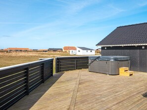 A wooden deck with a hot tub and wooden steps, surrounded by a fence and a building with a dark roof. - Holiday Home in HarboÃ¸re (Harboore)