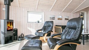 Ein gemütlicher Raum mit Kaminofen, Ledersesseln, einem kleinen Tisch und einem Fenster mit Blick.