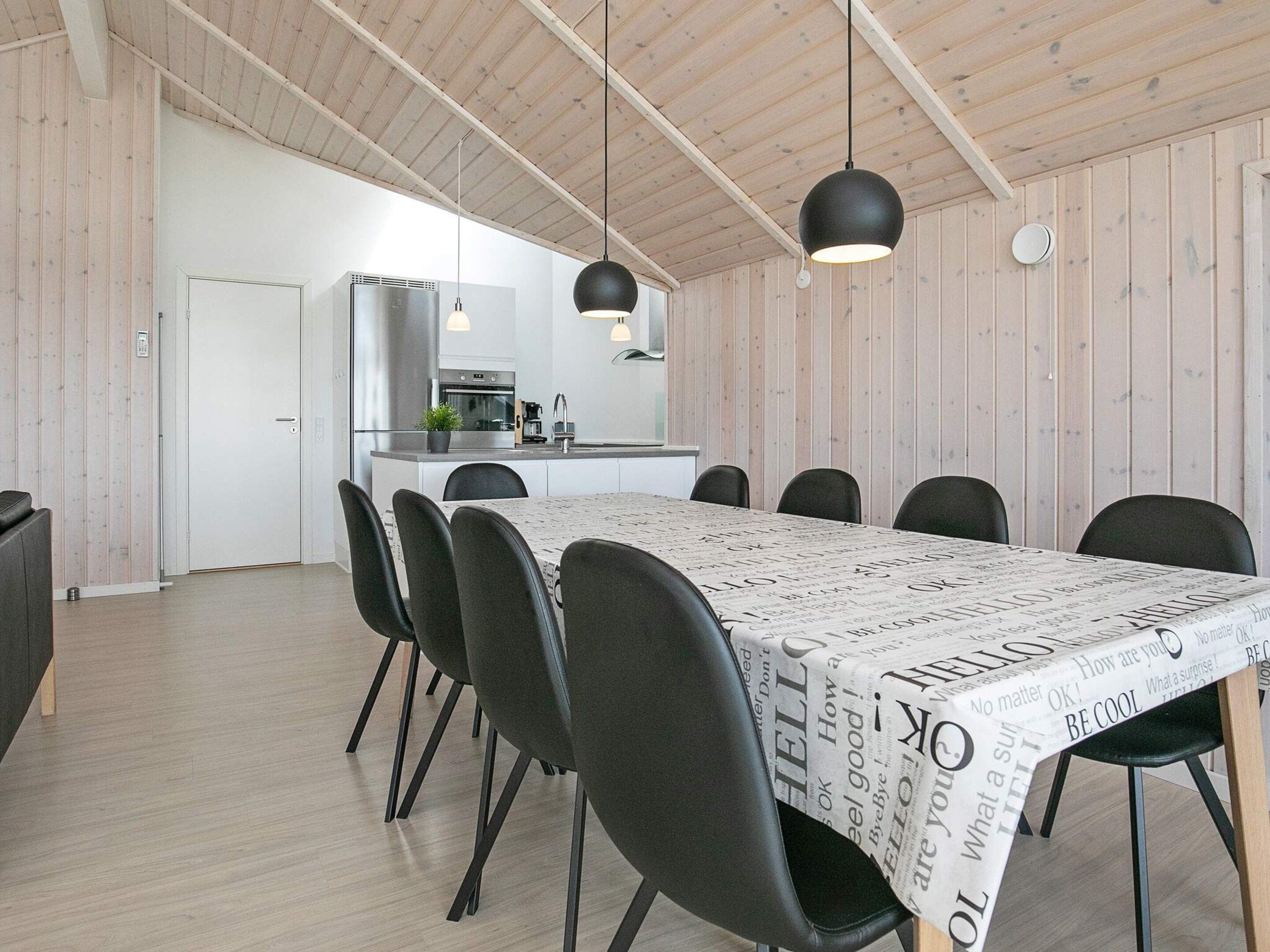 Een moderne eetruimte met een lange tafel, zwarte stoelen en hanglampen.