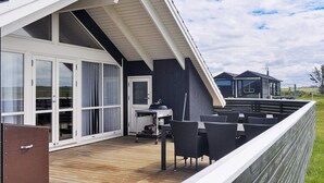 Eine Terrasse mit Gartenmöbeln, einem Grill und einer Glastür, die zu einem überdachten Bereich führt.