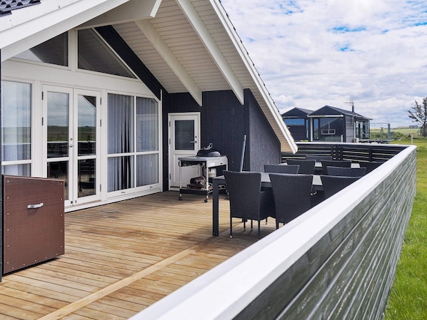 A deck with outdoor furniture and a grill, adjacent to a building with large windows and a door. - Holiday Home in HarboÃ¸re (Harboore)