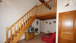 A wooden staircase leading to an upper level, a television on a wooden cabinet, a red sofa, and a wooden door.