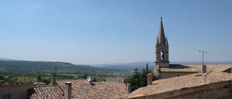A view of terracotta-tiled rooftops and a church tower with a spire, set against a clear sky.