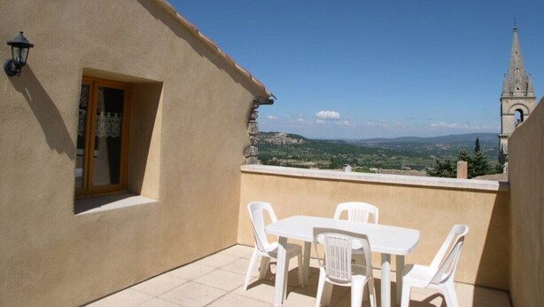 A balcony with a table and chairs, a window with a curtain, and a view of a distant church tower and landscape.