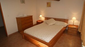 A bedroom with a wooden bed, two bedside tables with lamps, a wooden dresser, and a small painting on the wall.