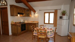 A kitchen with wooden cabinets, a tiled backsplash, a dining table with chairs, and a refrigerator.