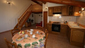 A dining area with a wooden staircase, a kitchen with wooden cabinets, and a tiled backsplash.