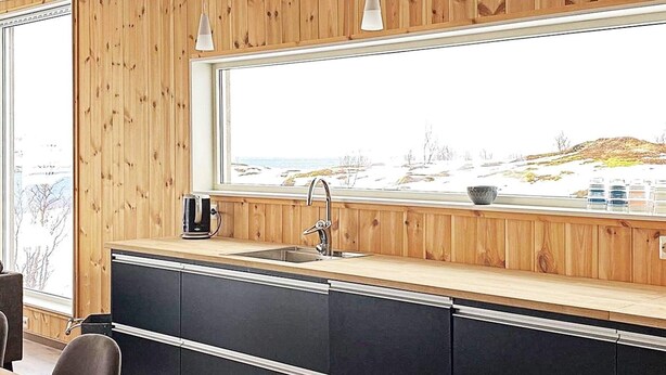 Cozinha moderna com painéis de madeira, uma janela grande e vista para uma paisagem nevada.