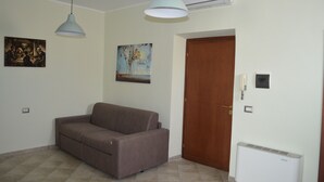 Una sala de estar con un sofá marrón, dos lámparas colgantes, una puerta y un aire acondicionado.