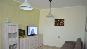 Una sala de estar con una televisión sobre un mueble de madera, un sofá marrón y dos lámparas colgantes.