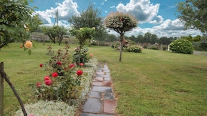 A garden pathway with a stone border, surrounded by lush greenery and flowering plants. - Family Home with Garden Near Mont St Michel - 3BR, 2BA, WiFi, Baby Gear, Linens Included (Céaux)