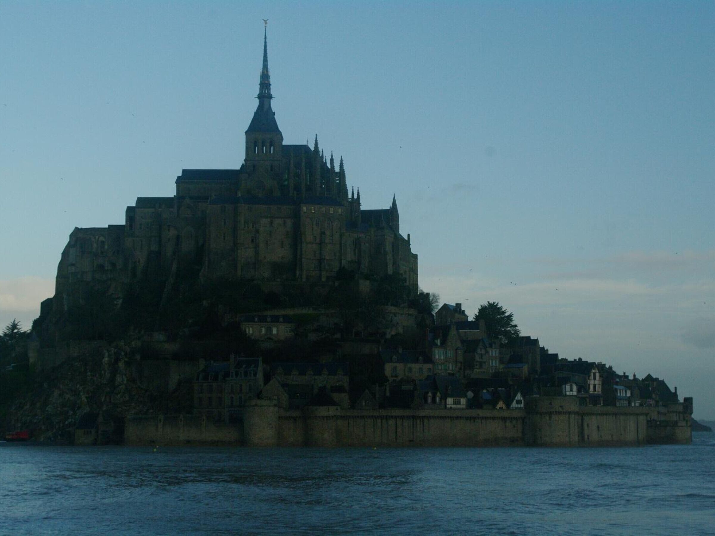 Une vaste structure imposante, digne d’un château historique, avec une tour remarquable, située sur une falaise surplombant une étendue d’eau.