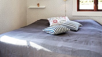Un dormitorio con cama, almohadas, mesita de noche, lámpara de pared y ventana con vista a árboles.