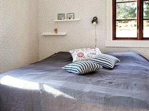 A bedroom with a bed, pillows, a nightstand, a wall-mounted lamp, and a window with a view of trees. - 4 Star Holiday Home in Skillingaryd (Skillingaryd)