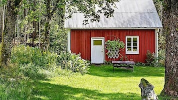 Una casa de madera roja con puerta y ventana blancas, rodeada de un patio cubierto de césped y árboles.