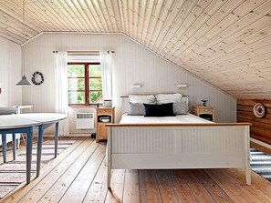 A bedroom with a sloped ceiling, a bed with white bedding, a bedside table, a lamp, and a window with curtains. - 4 Star Holiday Home in Skillingaryd (Skillingaryd)