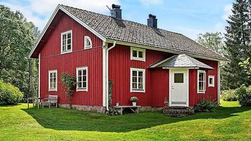 A red two-story house with a sloped roof, a front porch, and a well-maintained lawn.
