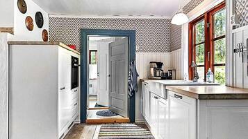 Una cocina con armarios blancos, piso de madera, alfombra colorida y ventana con vistas a zonas verdes.