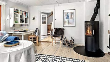 A cozy living room with a fireplace, a bookshelf, a dining area, and a staircase leading to another level.
