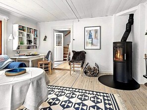 A cozy living room with a fireplace, a bookshelf, a dining area, and a staircase leading to another level. - 4 Star Holiday Home in Skillingaryd (Skillingaryd)