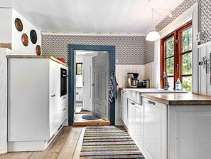 A kitchen with white cabinets, a wooden floor, a colorful rug, and a window with a view of greenery. - 4 Star Holiday Home in Skillingaryd (Skillingaryd)