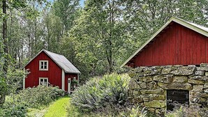 Ein rotes Bauernhaus mit Mauerwerk aus Stein und ein kleineres rotes Gebäude in einem bewaldeten Gebiet.