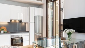 Une cuisine moderne avec des meubles blancs, un réfrigérateur en acier inoxydable et une table à manger en verre, accompagnée de chaises.