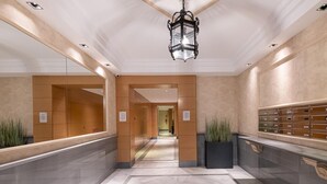 Un hall d’hôtel moderne avec un sol en marbre, des panneaux en bois, un couloir central et une rangée de casiers sur le côté droit.