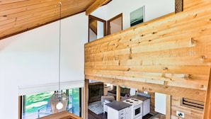 A modern kitchen with wooden beams, a stove, and a dining area with a view of the outdoors. - Cozy Updated Sunriver Cabin, 6 SHARC Passes, Floor to Ceiling Windows, Golf, Swim, Ski, and Explore (Sunriver)
