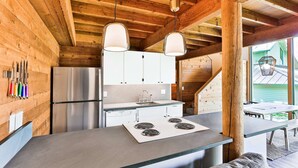 A modern kitchen with wooden walls, a stainless steel refrigerator, white cabinets, a built-in stove, and pendant lighting. - Cozy Updated Sunriver Cabin, 6 SHARC Passes, Floor to Ceiling Windows, Golf, Swim, Ski, and Explore (Sunriver)