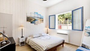 Un dormitorio con cama, dos mesitas de noche, un aparador, una ventana con vistas y un cuadro en la pared.