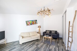 A living room with a beige sofa, a dark grey sofa, a wooden coffee table, a floor lamp, and a unique chandelier.