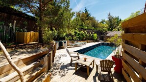 Terraza de madera con piscina, sillas de descanso y una pequeña mesa.
