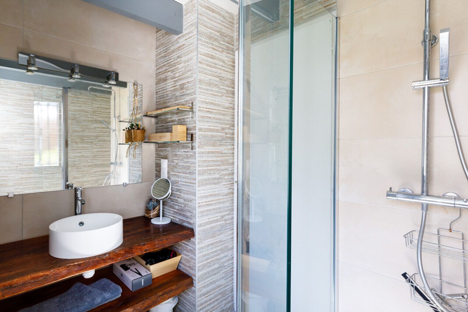 A modern bathroom with a large mirror, a white sink, and a glass-enclosed shower.