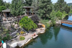 A lakeside property with a wooden deck, outdoor seating, and a small pavilion.