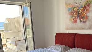 Ett sovrum med en röd sänggavel, två sängar med randiga sängkläder, ett stort fönster och en färgstark målning av en fjäril på väggen.