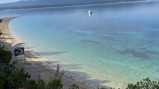 En strand med klart vatten, en båt och berg i fjärran.
