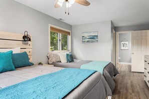Een slaapkamer met twee bedden, een raam, een plafondventilator en een deur.