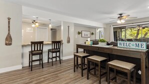 A modern kitchen with a bar area, wooden chairs, and a 'WELCOME' sign. - Knolls 0424 - Three Bedroom Apartment, Sleeps 8 (Osage Beach)