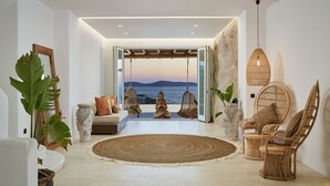 A spacious room with a large woven rug, wicker chairs, and a view of the sea. - Ubud Mykonos (Mykonos)