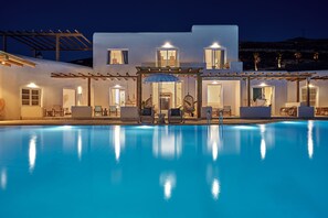 Un edificio moderno con piscina, asientos exteriores y una pérgola.