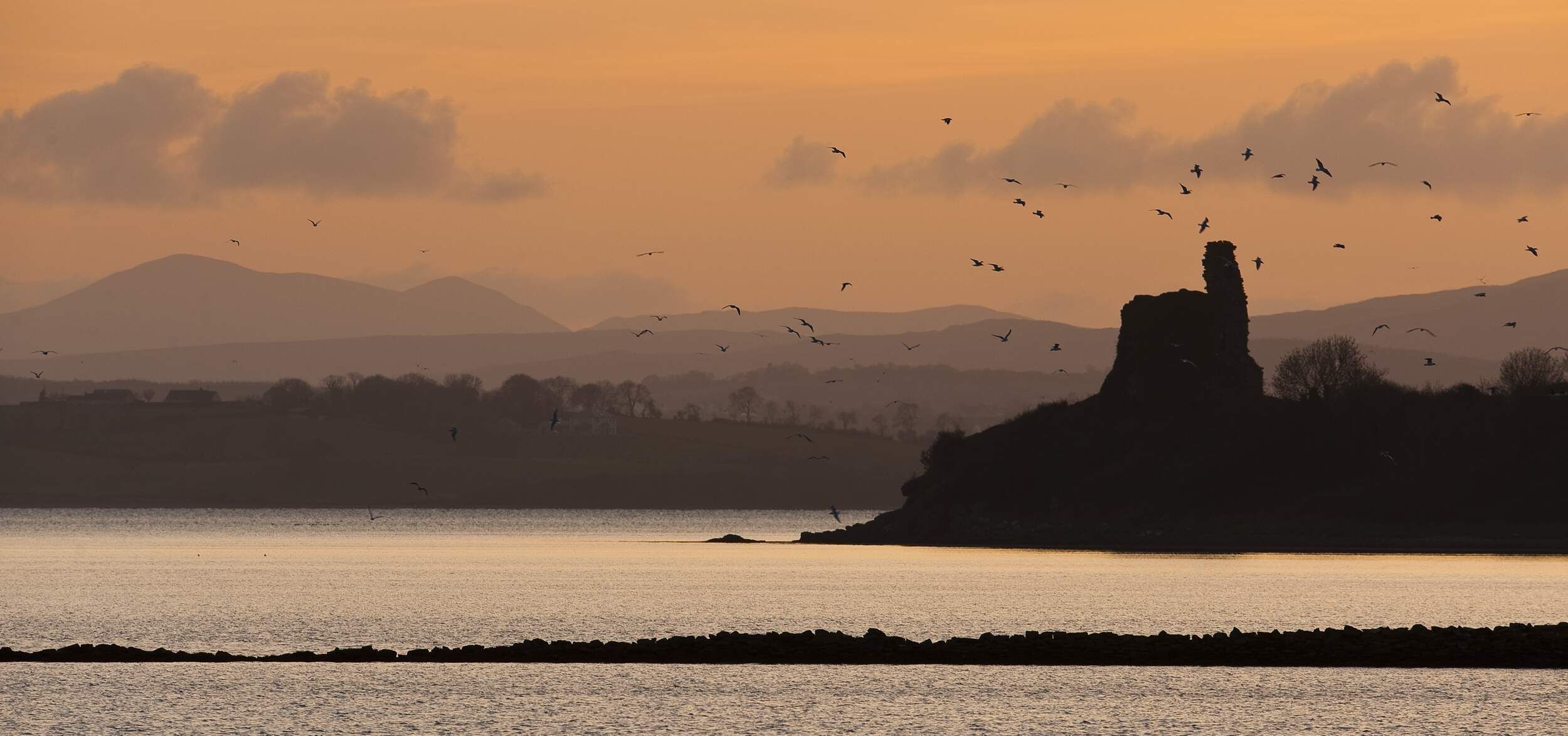 A coastal landscape with a prominent rock formation silhouetted against a sunset.