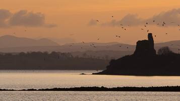 A coastal landscape with a prominent rock formation silhouetted against a sunset.